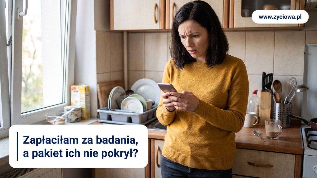 Kobieta stoi w kuchni z telefonem w dloni, z wyrazem zaskoczenia na twarzy.